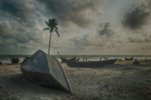 Tranquil beach scene with wooden boats, palm tree, and cloudy sky in Cox's Bazar.