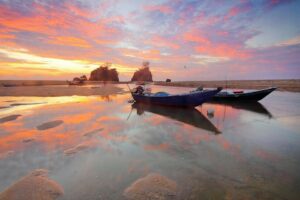 Serene beach scene at sunset with boats and vibrant sky reflections.