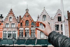 A hand holding a miniature Bruges building with traditional Belgian architecture in the background.