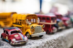 Close-up of vintage toy cars and buses arranged on concrete with a blurred background.