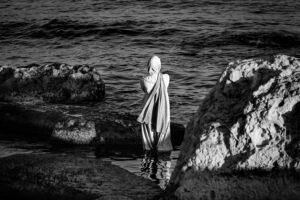 Black and white photo of a solitary person by sea rocks in Aktau, Kazakhstan.