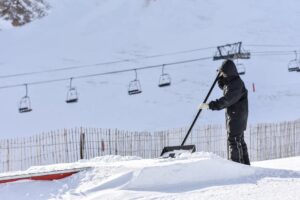Person shoveling snow at Arinsal ski resort during winter under ski lift.