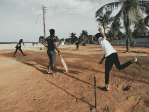 A group of young men playing cricket on a sandy beach under clear skies.