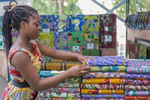 Young woman arranging colorful fabrics at a market in Cotonou, Benin, showcasing vibrant African prints.