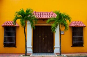 A colorful Colombian house facade with palm trees and a wooden door.